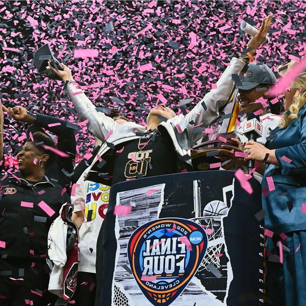 woman stands in a shower of confetti with hands raised to the ceiling